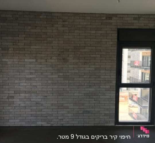 קיר לבנים אפור וחלון גדול בחדר ריק